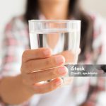 Happy beautiful young woman holding drinking water glass in her hand. Health care concept.
