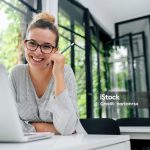 Portrait of smiling young female student in eyeglasses sitting in modern library.
