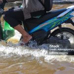 Banjarmasin, Indonesia - December 9, 2021: Banjarmasin residents use cars, motorbikes to walk across the flooding street in Sultan Adam, Banjarmasin, Indonesia.