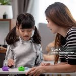 Asian mother and daughter play modeling clay together in kitchen with day light and they look happy. Concept of enjoy with family time