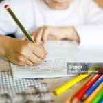 Child doing homework and writing story essay. Elementary or primary school class. Closeup of hands and colorful pencils.