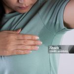 Close-up asian woman with hyperhidrosis sweating. Young asia woman with sweat stain on her clothes against grey background. Healthcare concept.