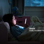 A child using smart phone lying in bed late at night, playing games, watching videos online, scrolling screen. Children's screen addiction. Child's room at night.